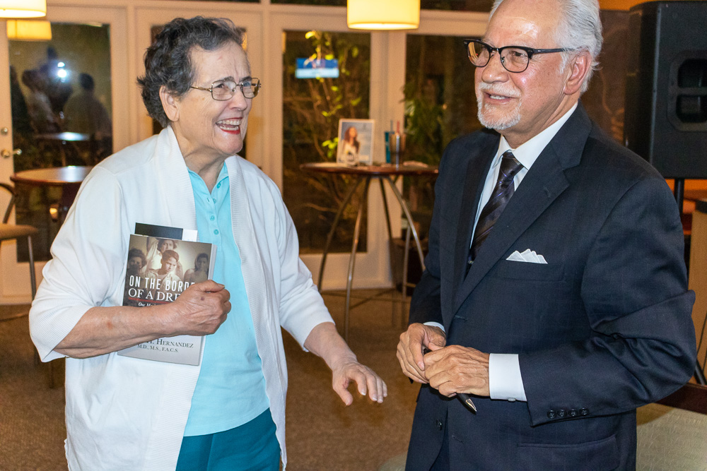 A woman holding a book talks to Dr. Edgar Hernandez