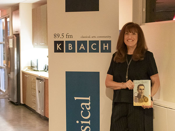 Author Jan Krulick-Belin stands in front of a KBACH pull-up banner holding her book
