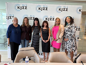 Six women pose in front of a step-and-repeat wall with the KJZZ logo